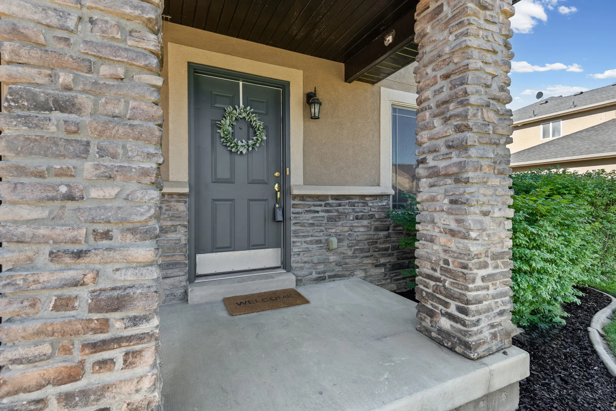 Stone veneer accents, concrete porch, dark paneled entry door, exterior wall lantern