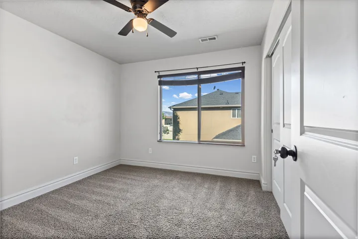 Wall-to-wall carpeting, ceiling fan with integrated lighting, sliding closet doors, and a window with roller shades