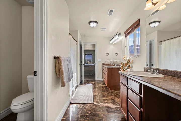 Dual wood-finish vanities with integrated sinks, expansive wall-mounted mirrors, and an adjacent water closet