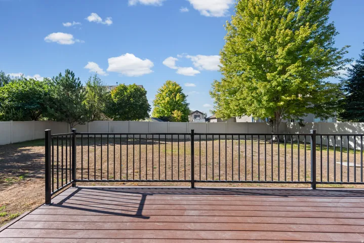 Wood-finish deck with a black metal railing, featuring a large backyard with a privacy fence and mature trees