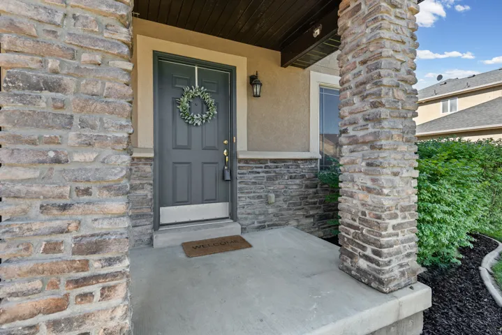 Stone veneer accents, concrete porch, dark paneled entry door, exterior wall lantern