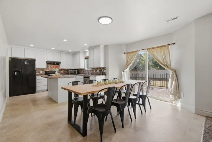 Tile flooring, white cabinetry, stone backsplash, stainless steel appliances, and sliding glass door