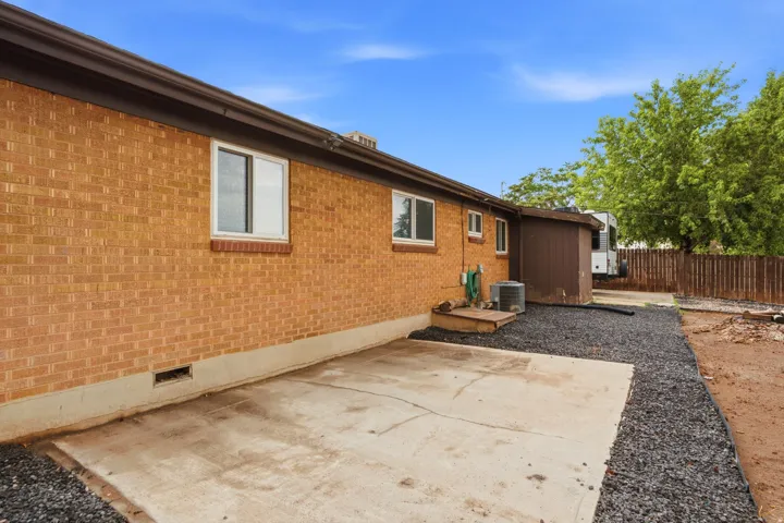 Brick exterior with concrete patio, RV parking, and gravel pathway, complemented by landscaping and wooden fencing