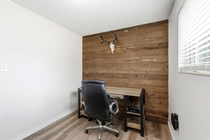 Distinguished accent wall featuring wood paneling, complementing wood-finish flooring, and a window with horizontal blinds