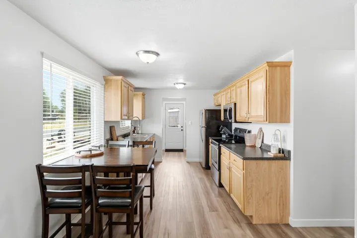 Open-concept kitchen and dining area featuring natural wood cabinetry, black electric range, wood-finish flooring, and abundant natural light