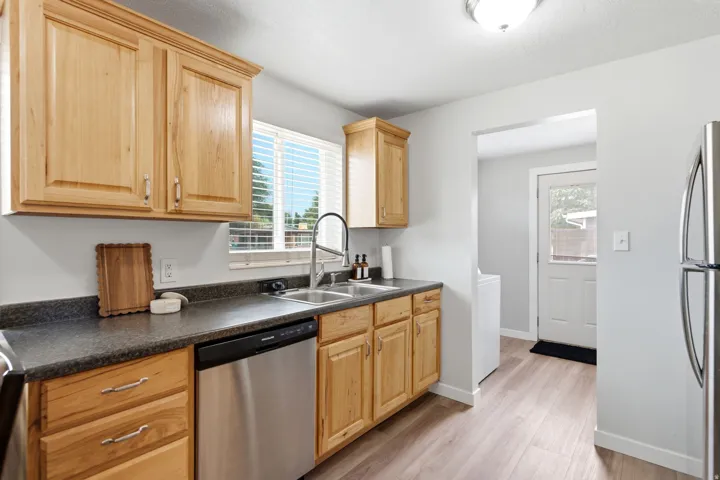 Kitchen featuring wood cabinetry, a stainless steel dishwasher, a double basin sink with a high-arc faucet, and light wood-finish flooring