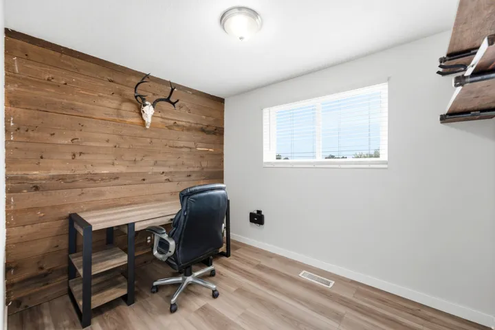 Wood-finish flooring, accent wall with horizontal wood paneling, and a single window with blinds