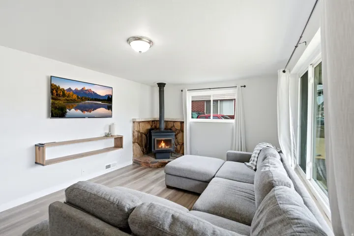 Bright living room showcasing plank-style wood-finish flooring, a wood-burning stove with decorative surround, and expansive glazed doors and windows providing natural light