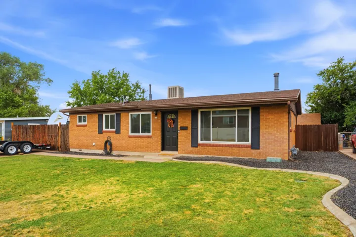 Brick exterior, dark brown roof, dark shutters, front door with decorative glass, and a landscaped front yard