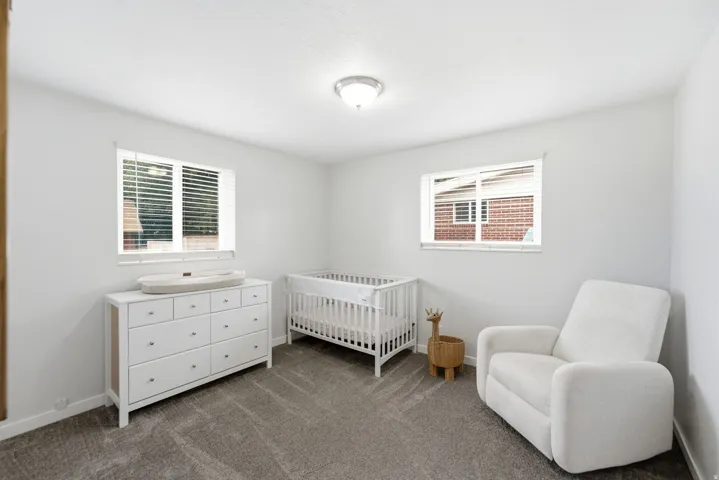 Bright bedroom featuring dual windows with blinds, neutral carpeting, and ceiling lighting