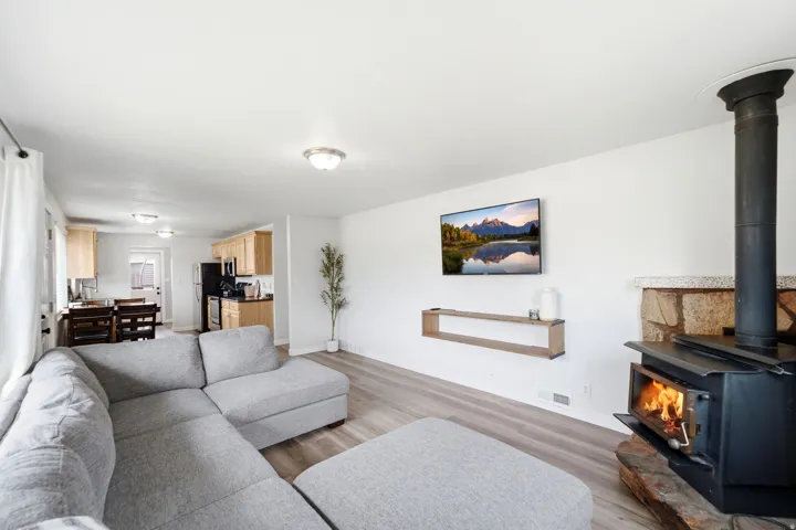 Open-concept living area featuring engineered wood-finish flooring, a wood-burning stove with black metal surround, and recessed ceiling lighting