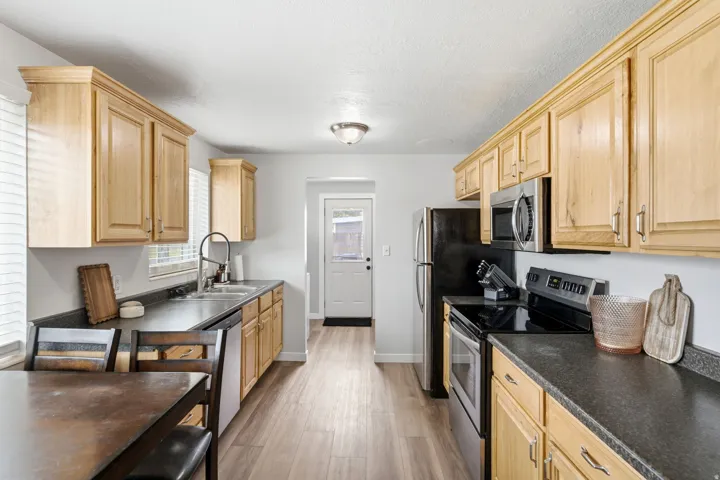 Galley kitchen showcasing natural wood cabinetry, dark countertops, stainless steel appliances, and wood-finish flooring
