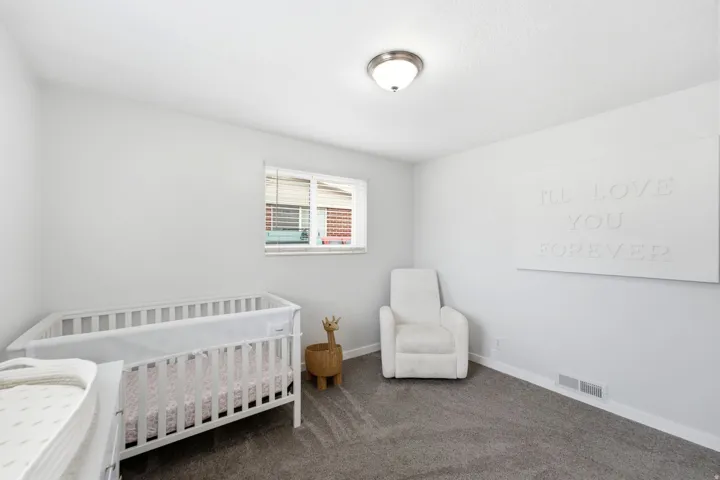 Bright bedroom featuring dual windows with blinds, neutral carpeting, and ceiling lighting