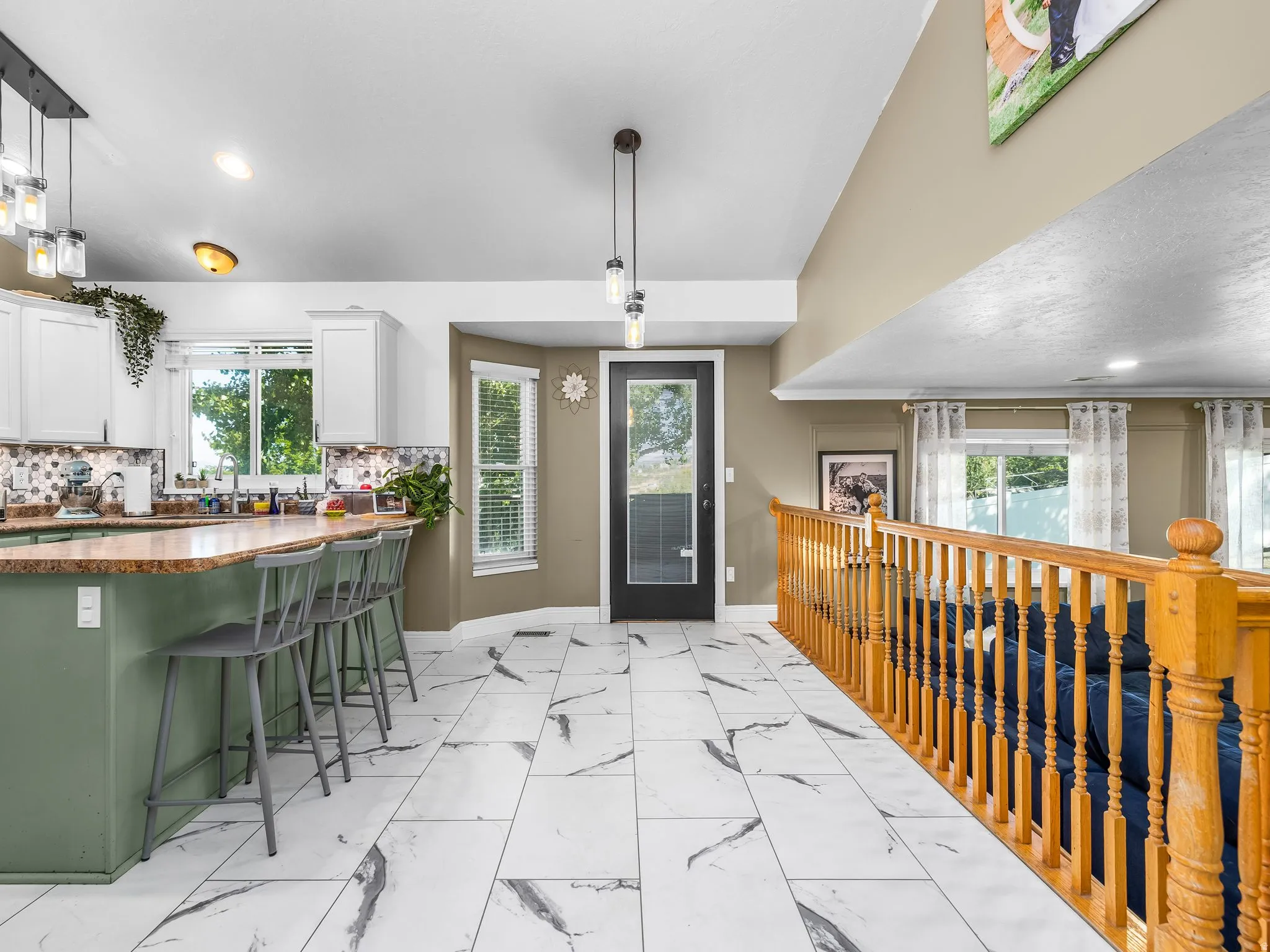 Spacious open concept design featuring large format tile flooring, a kitchen island with a stone-finish countertop, white cabinetry with a tile backsplash, and a wood railing