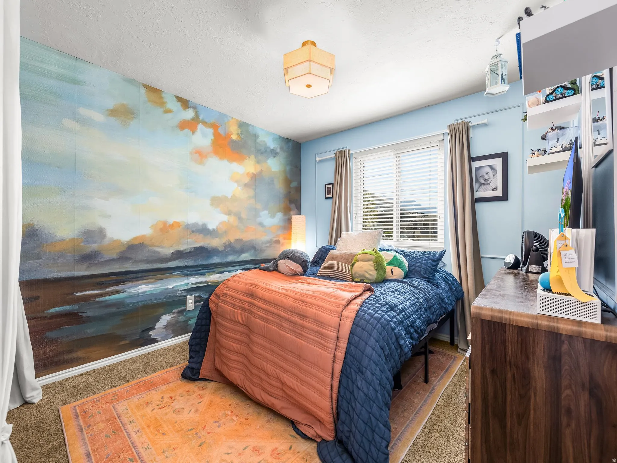 Accent wall with a serene mural, window with horizontal blinds, built-in shelving, and wood-finish dresser