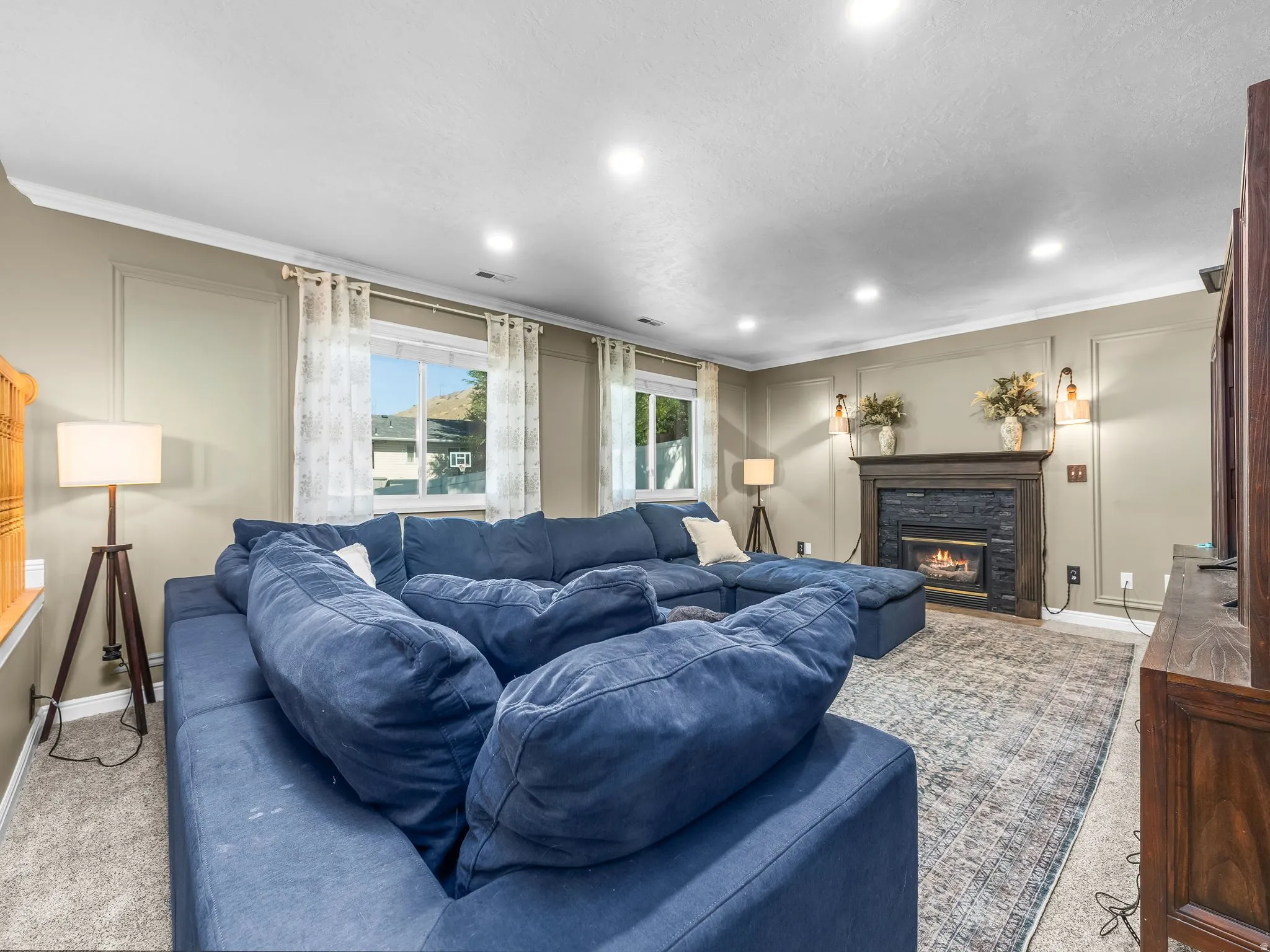 Recessed ceiling lighting, crown molding, double windows with trim, a built-in fireplace with a stone surround, and wall sconces