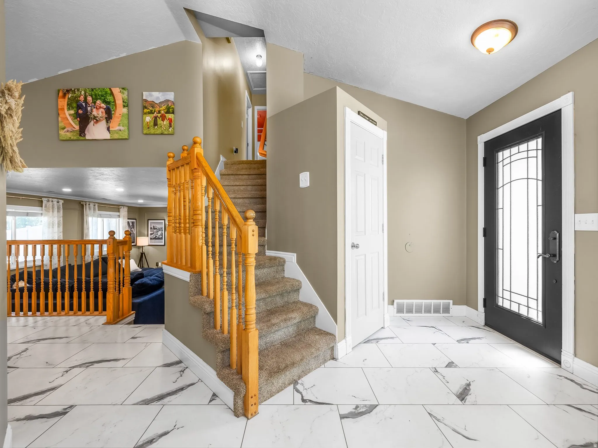 White tile flooring with dark veining, a carpeted staircase with wood banister, a paneled door, and a front entry door with decorative glass inserts
