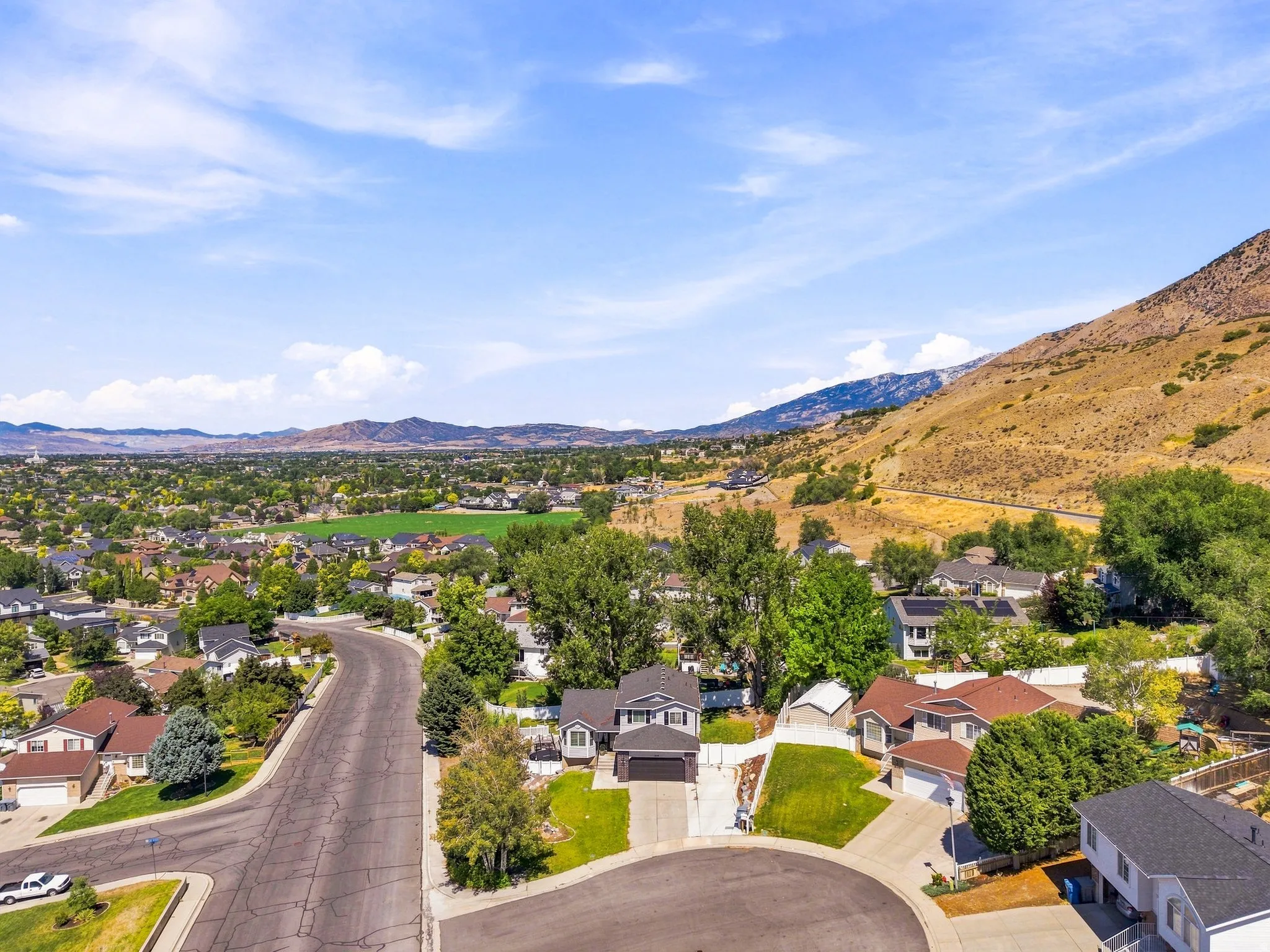 Residential street with cul-de-sac, surrounded by mature trees and distant mountains, featuring a single-family home with an attached garage