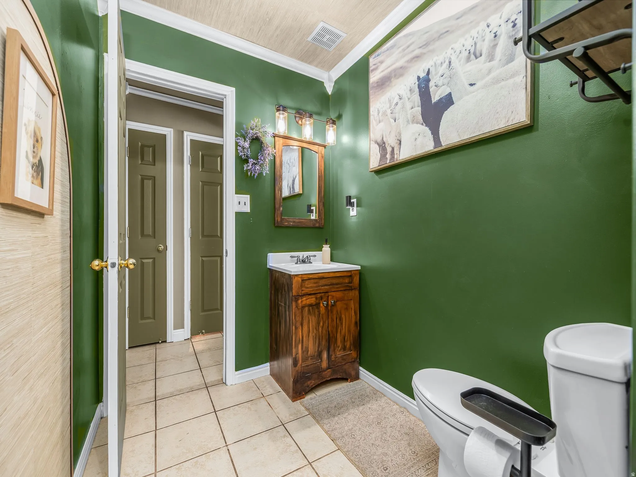 Tile flooring, wood-finish vanity with countertop and integrated sink, wall-mounted vanity lighting, and a toilet