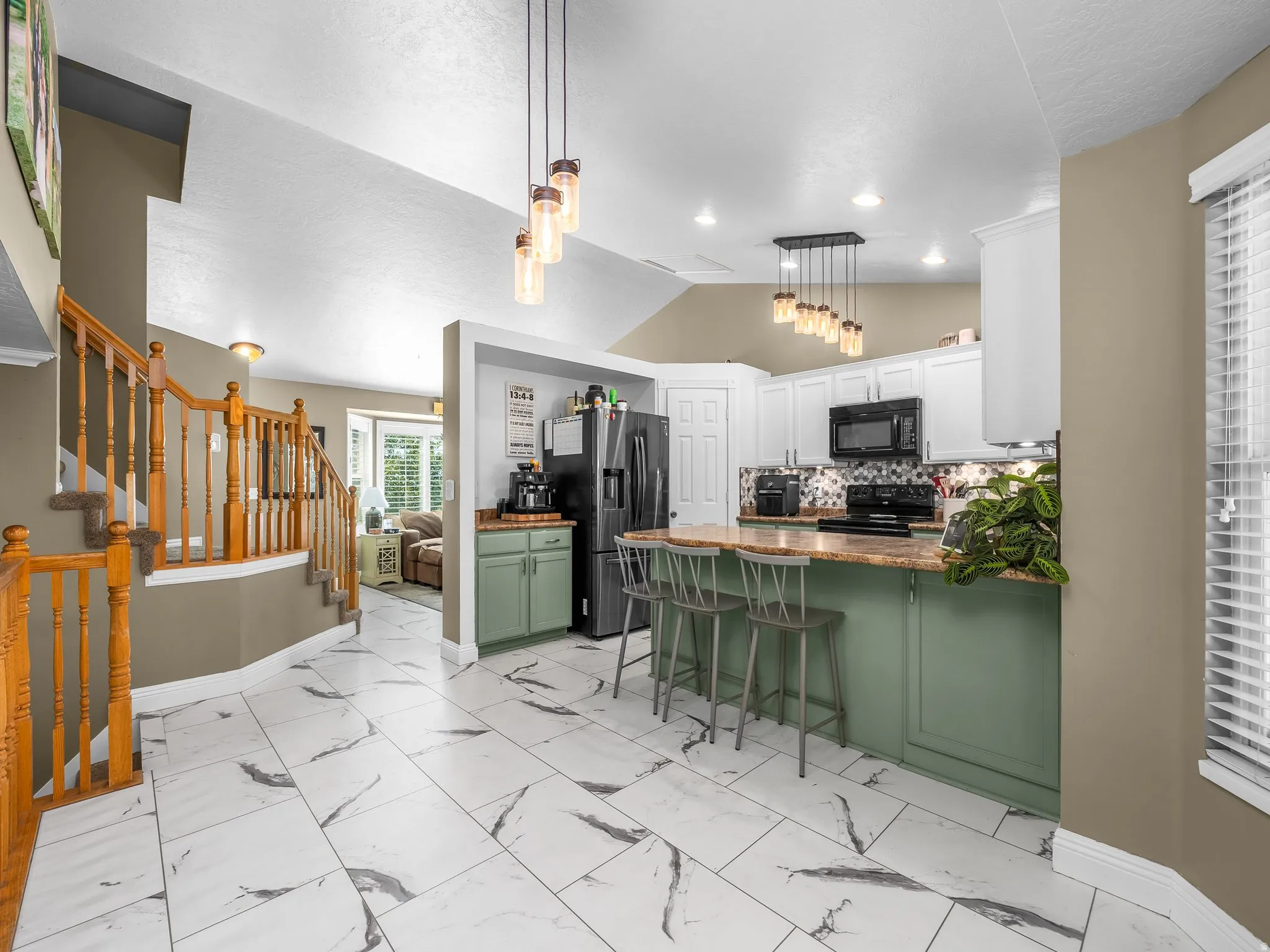 Open-concept layout featuring a kitchen with white cabinetry, a kitchen island with a natural wood-finish countertop, and decorative pendant lighting fixtures