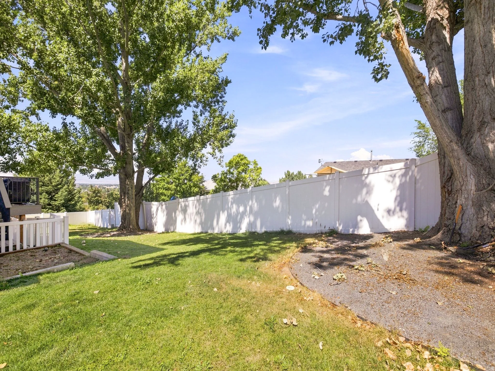 Expansive yard featuring mature trees, a manicured lawn, and a white privacy fence
