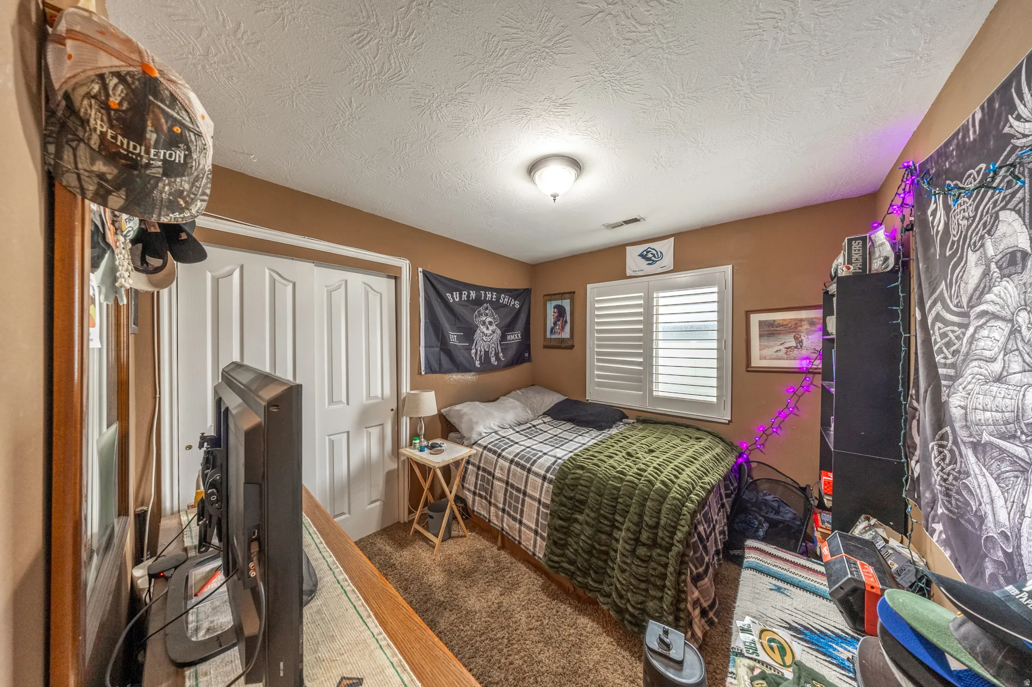 Bedroom #1 features comfortable carpeting, a ceiling-mounted light fixture, classic white plantation shutters, and a closet with bifold doors.