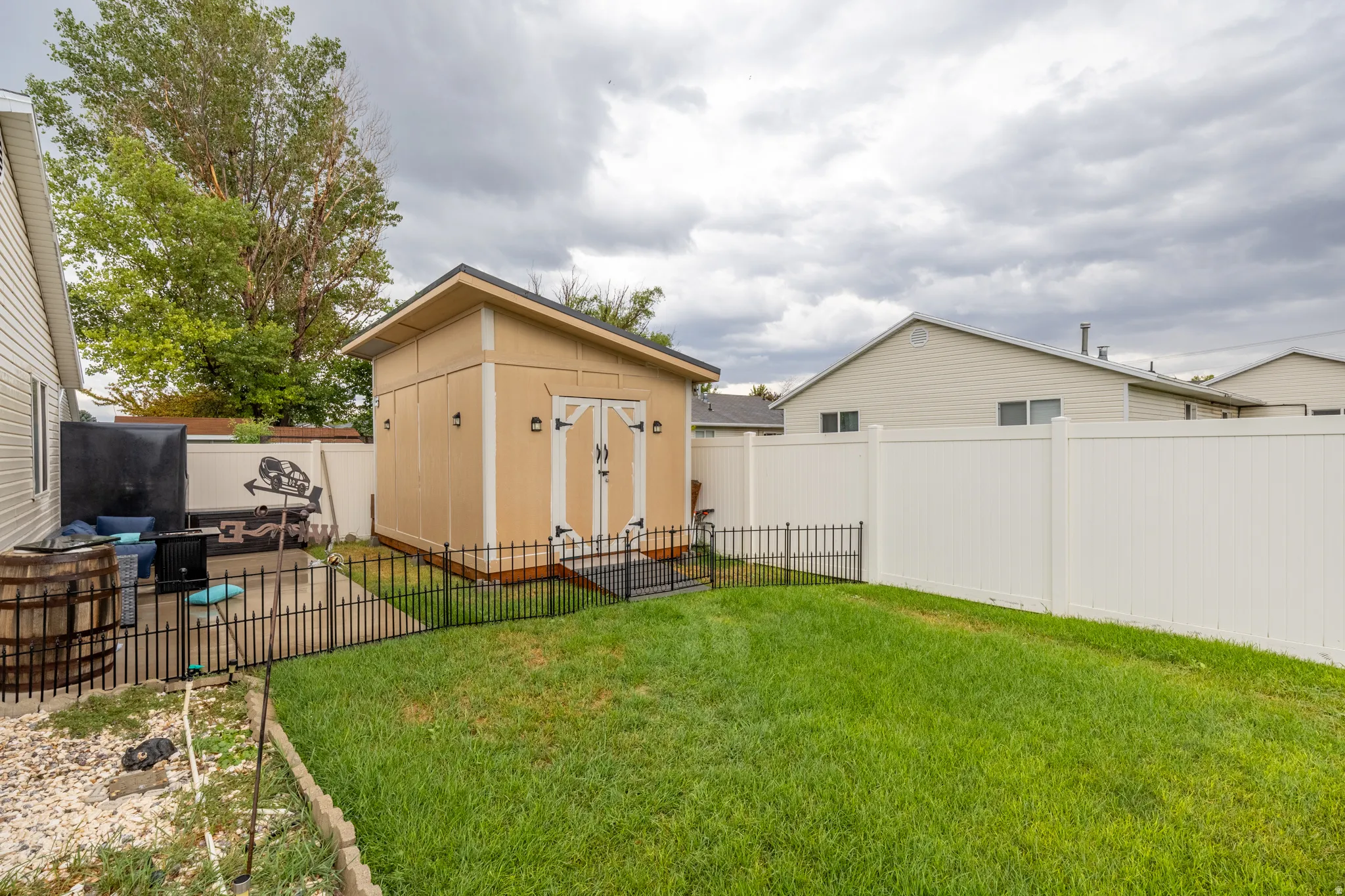 Beautifully maintained outdoor space featuring a manicured lawn, durable vinyl fencing, patio area, wrought iron-style fencing, and a large custom-built storage shed offering exceptional space for tools, equipment, and additional storage.