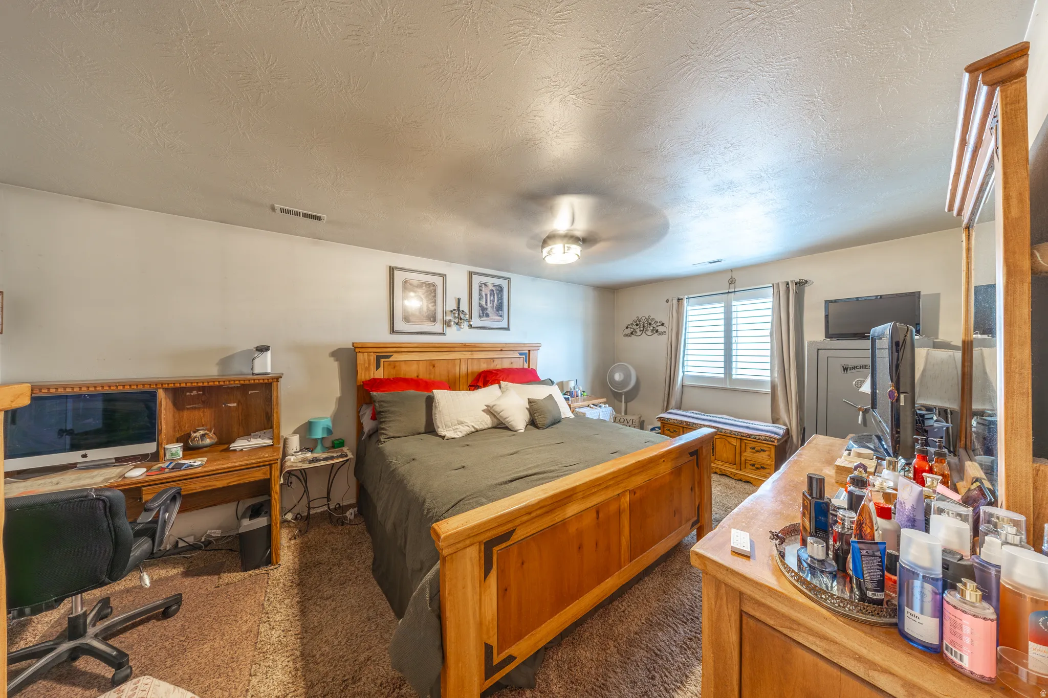 Spacious primary bedroom offering generous room for a full bedroom suite, featuring plush carpeting, a ceiling fan, and a large window with classic white plantation shutters that provides abundant natural light. The primary suite also includes a private e