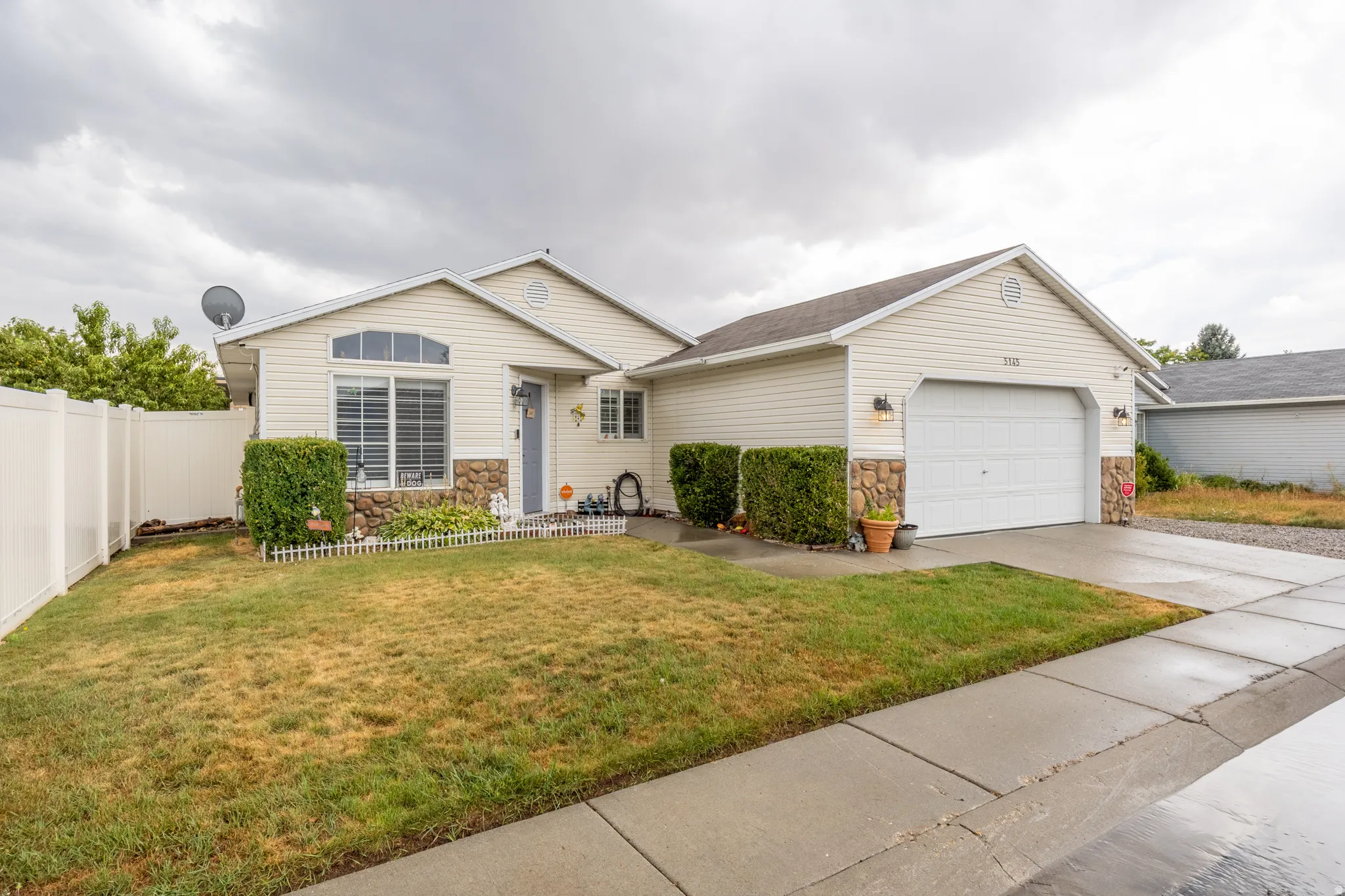 Inviting single-story home featuring light-colored siding, attractive stone accents, and an attached two-car garage.