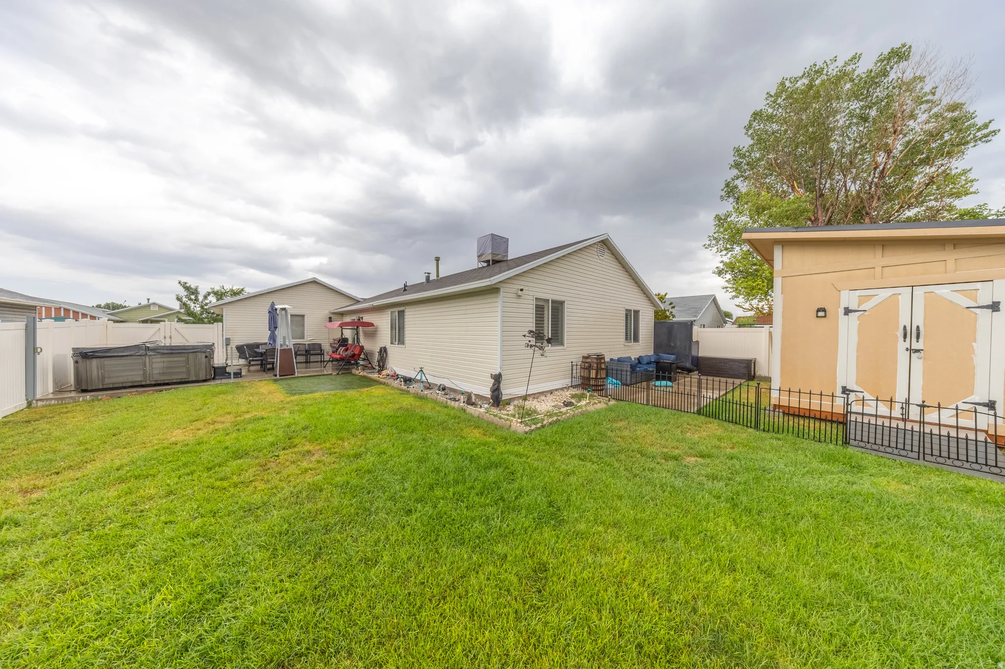 Beautifully maintained exterior featuring a manicured lawn, light-colored siding, white vinyl and black metal fencing, and a large custom-built storage shed with double doors providing ample additional storage.