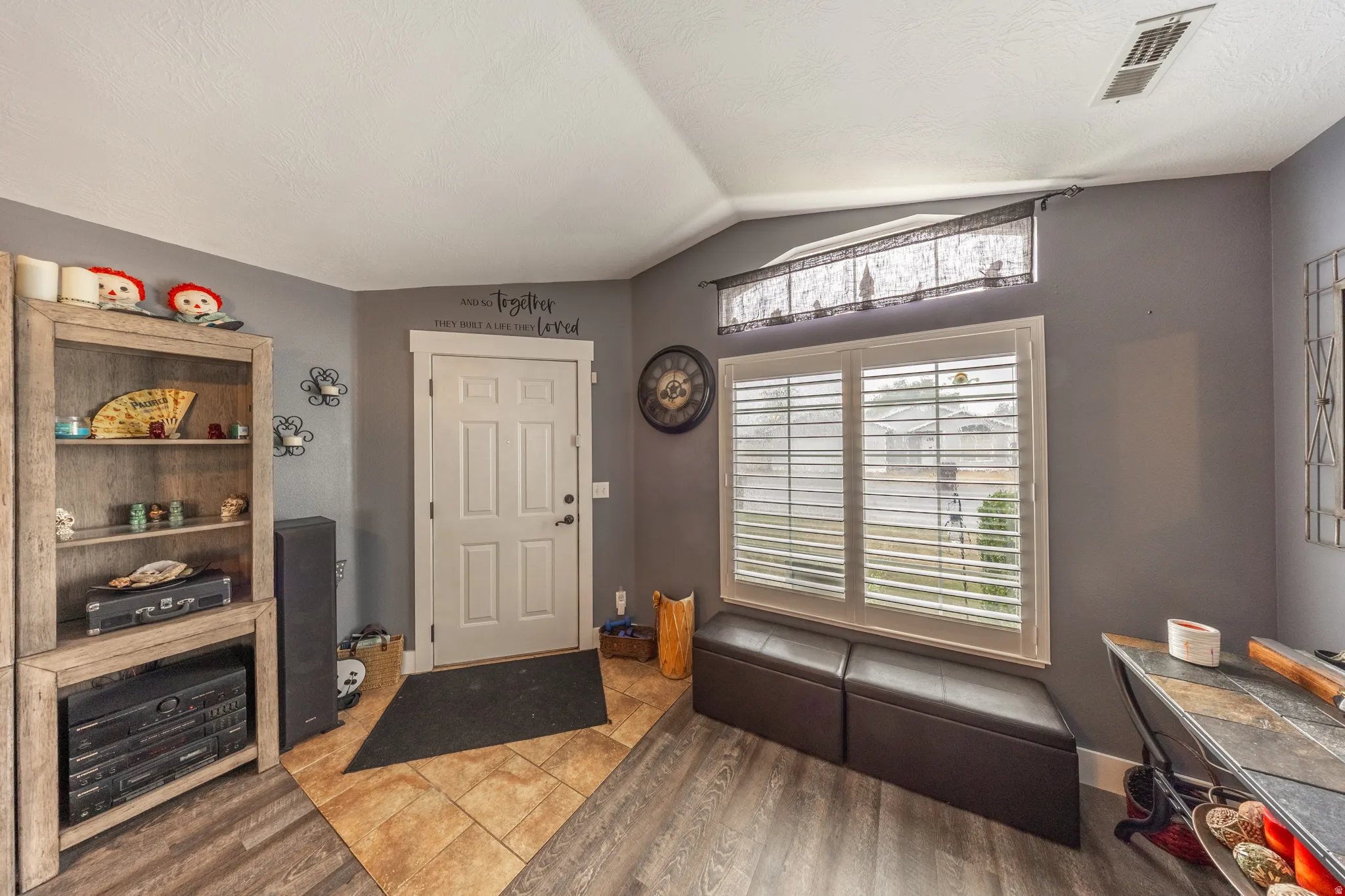 Welcoming entry featuring a solid-core paneled door, a tasteful combination of wood-look plank and ceramic tile flooring, and a window accented with classic plantation shutters.