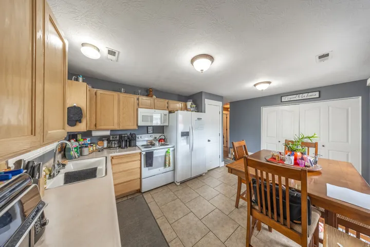 Bright and inviting kitchen featuring light wood cabinetry, crisp white appliances, a white sink, and durable tile flooring.