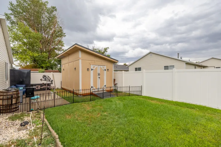 Beautifully maintained outdoor space featuring a manicured lawn, durable vinyl fencing, patio area, wrought iron-style fencing, and a large custom-built storage shed offering exceptional space for tools, equipment, and additional storage.