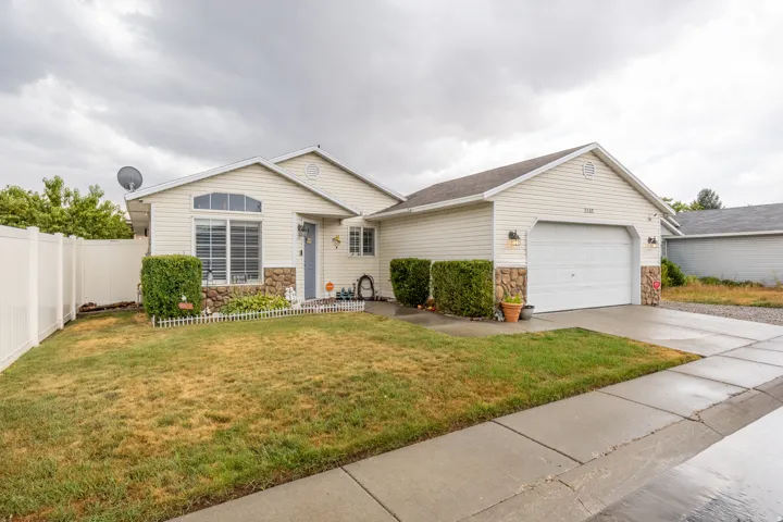 Inviting single-story home featuring light-colored siding, attractive stone accents, and an attached two-car garage.