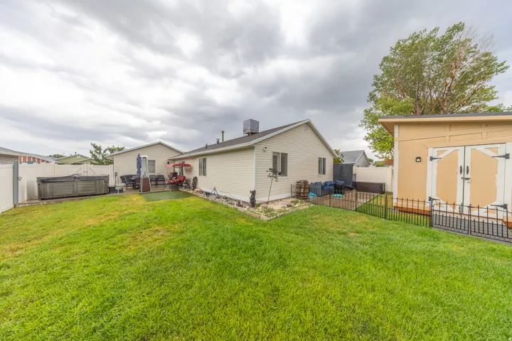 Beautifully maintained exterior featuring a manicured lawn, light-colored siding, white vinyl and black metal fencing, and a large custom-built storage shed with double doors providing ample additional storage.