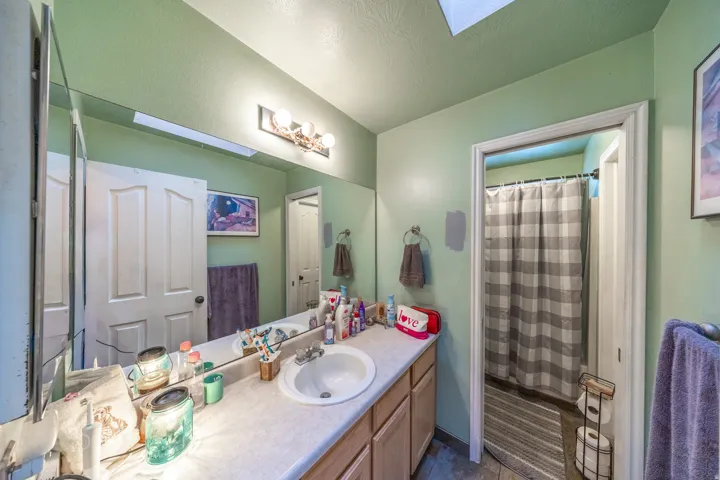 Bright and spacious primary bathroom featuring a dual-sink vanity with generous countertop space and storage, a large framed mirror, and a skylight that fills the space with natural light.