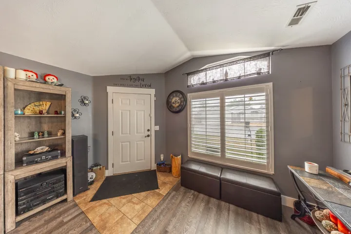 Welcoming entry featuring a solid-core paneled door, a tasteful combination of wood-look plank and ceramic tile flooring, and a window accented with classic plantation shutters.