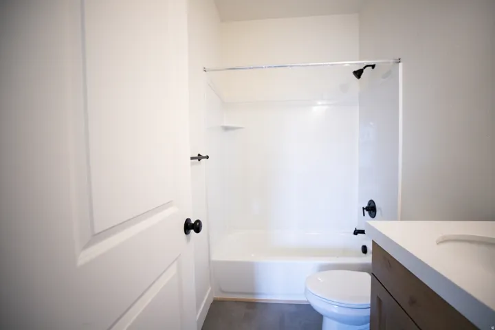 Full secondary bath with stained wood cabinets and quartz slab countertops.