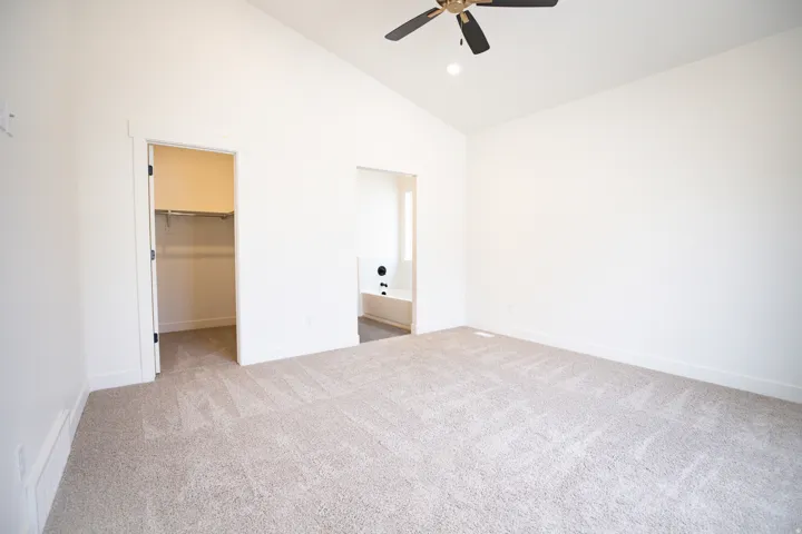Primary bedroom with vaulted ceiling, ceiling fan and adjacent walk-in closet.