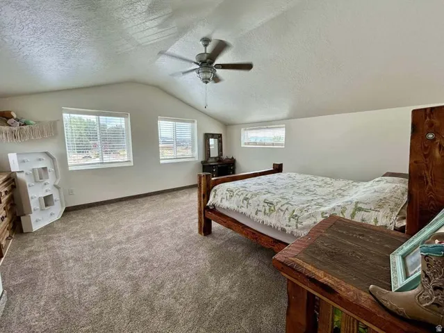 Vaulted ceiling with a ceiling fan, multiple windows with blinds, and carpeted flooring