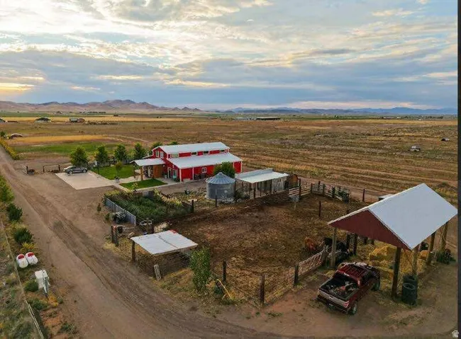 Red barn-style structure with white trim, a gravel driveway, and surrounding agricultural land
