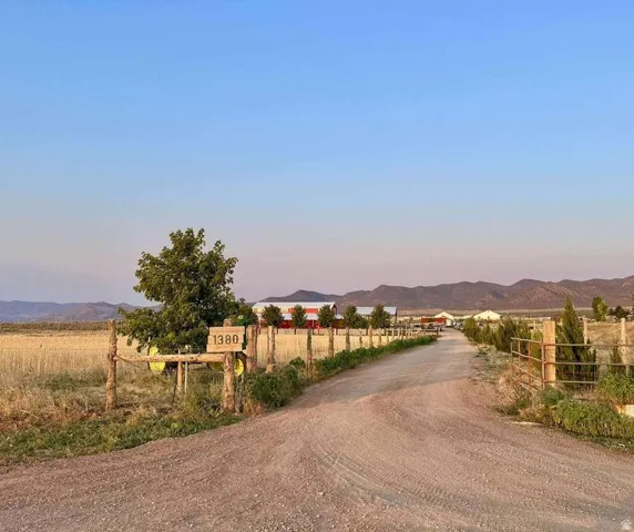 Gravel driveway with split rail fencing and mature trees, leading to a property with multiple red-roofed structures