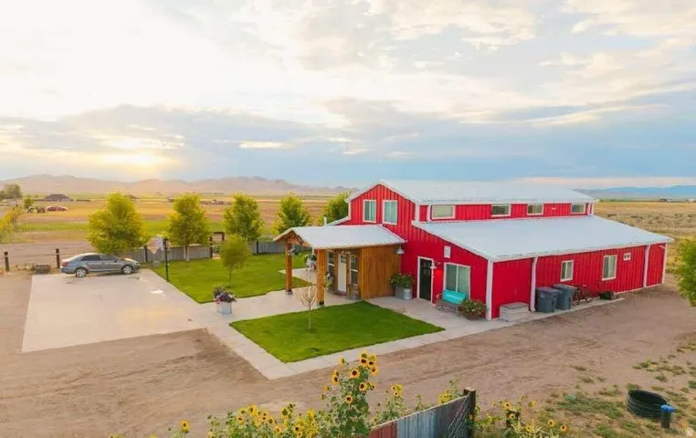Red exterior with white trim, metal roofing, covered porch with wood accents, concrete driveway, and a manicured lawn area