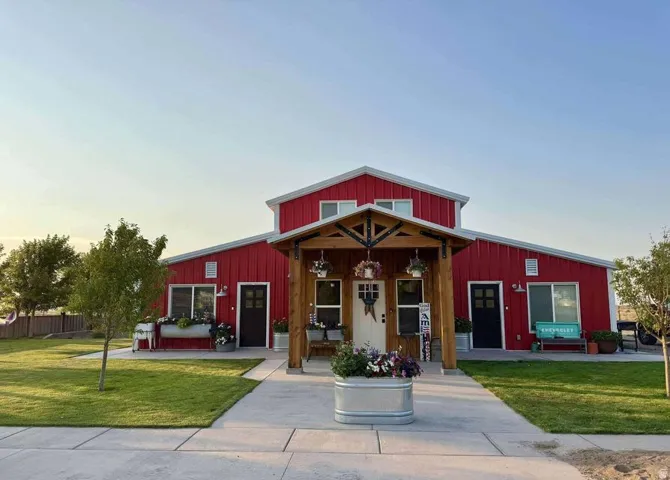Red exterior siding with white trim, covered front entry with natural wood beams, prominent front walkway, manicured lawn, and multiple windows