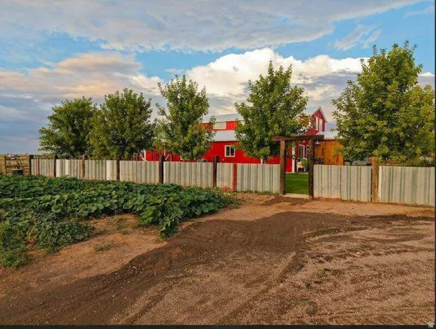 Red-sided barn structure with white trim, bordered by mature trees and a slatted fence