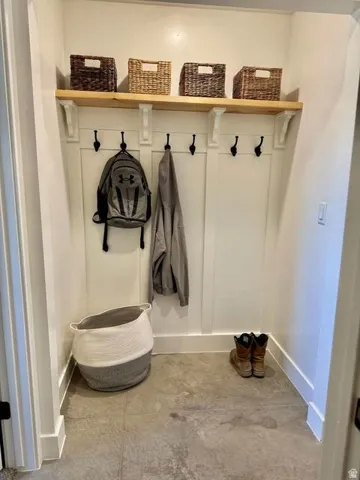 Organized entryway featuring a wood-finish shelf with woven storage baskets, black hook rail for coats and accessories, and concrete flooring