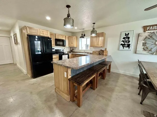 Kitchen featuring light wood cabinetry, a central island with a corrugated metal accent, dark-finish appliances, and recessed lighting