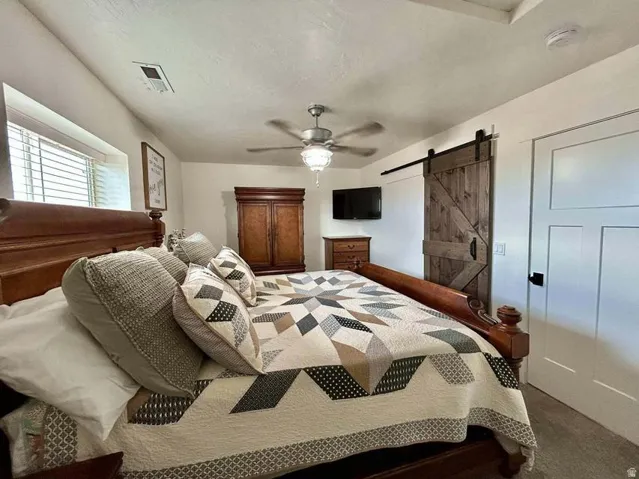Sliding barn door with black hardware, ceiling fan with light fixture, white interior door with black hardware, and an egress window