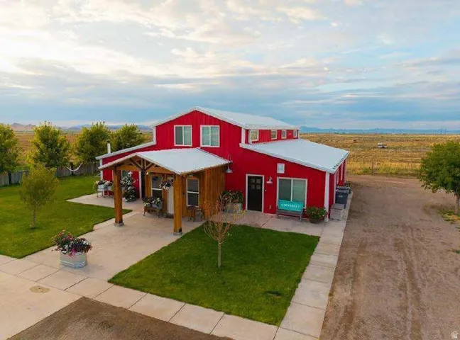 Red exterior with white trim, wood-clad entryway, multiple windows, concrete patio, and a grass lawn