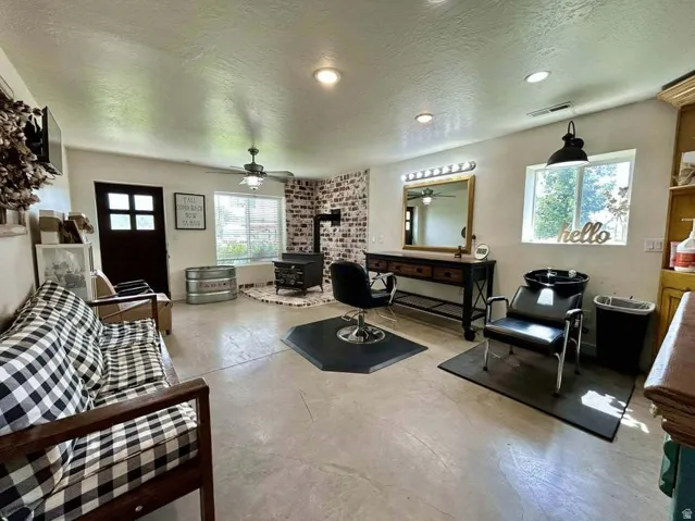 Exposed brick accent wall with a built-in wood-burning stove, concrete flooring, ceiling fan, and recessed lighting